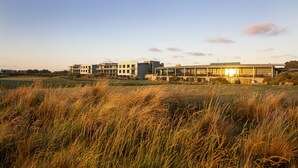 A modern building with a flat roof and large windows, surrounded by tall grass. - The Sands Torquay (Torquay)