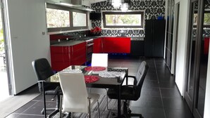 A modern kitchen with red and black cabinetry, a dining area with a table and chairs, and a view through the window. - Luxury Designer home on Beautiful Macleay Island, just 1 hour from Brisbane! (MacLeay Island)