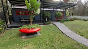 A modern house with a covered patio, a red planter with a large plant, and a well-maintained lawn. - Luxury Designer home on Beautiful Macleay Island, just 1 hour from Brisbane! (MacLeay Island)