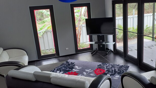 A living room with a flat-screen TV, a sofa, and a patterned rug. - Luxury Designer home on Beautiful Macleay Island, just 1 hour from Brisbane! (MacLeay Island)