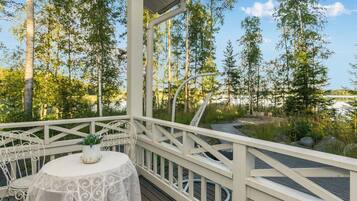 A covered outdoor deck with a table and chairs, surrounded by trees and a view of a lake.