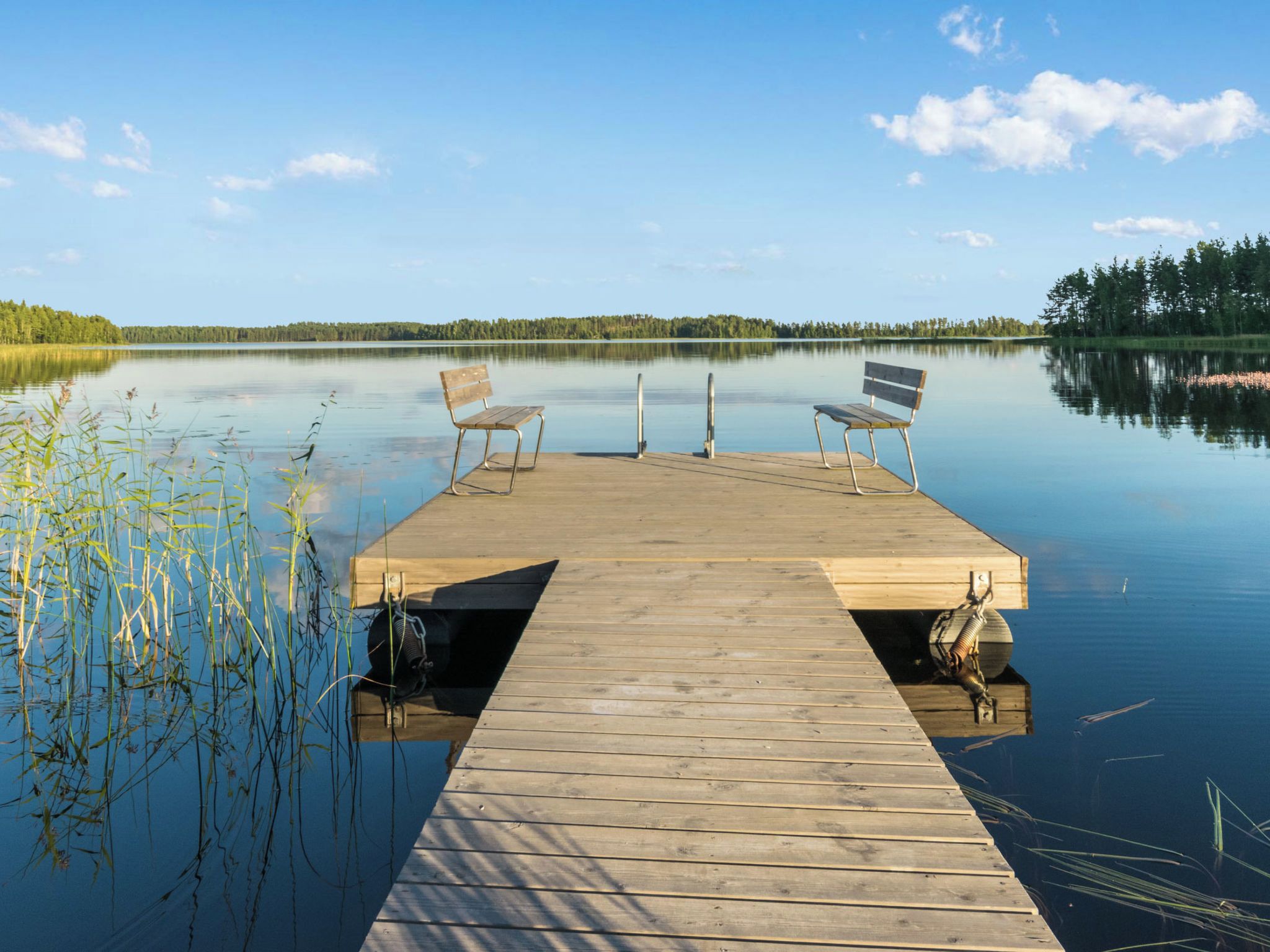 Puinen laituri, joka ulottuu tyynen veden ylle, ja sen päässä on kaksi penkkiä, joiden selkänojat ovat veden puolella.