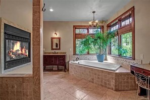 A spacious bathroom with a large bathtub, a fireplace, and a view of greenery through the windows. - Luxurious Chalet! Hot-tub, Bonfire & A+ Location for Skiing/Town (Ellicottville)