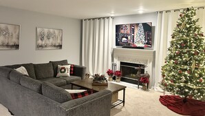 Ein Wohnzimmer mit grauem Sofa, Couchtisch, Kamin und Weihnachtsbaum.