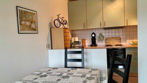 A compact kitchen with a dining area, featuring a bed with a patterned bedspread, a bicycle mounted on the wall, and a vintage radio.