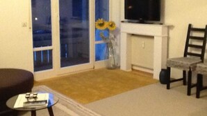 A living room with a television on a stand, a fireplace, and a large window with a view of the outside.