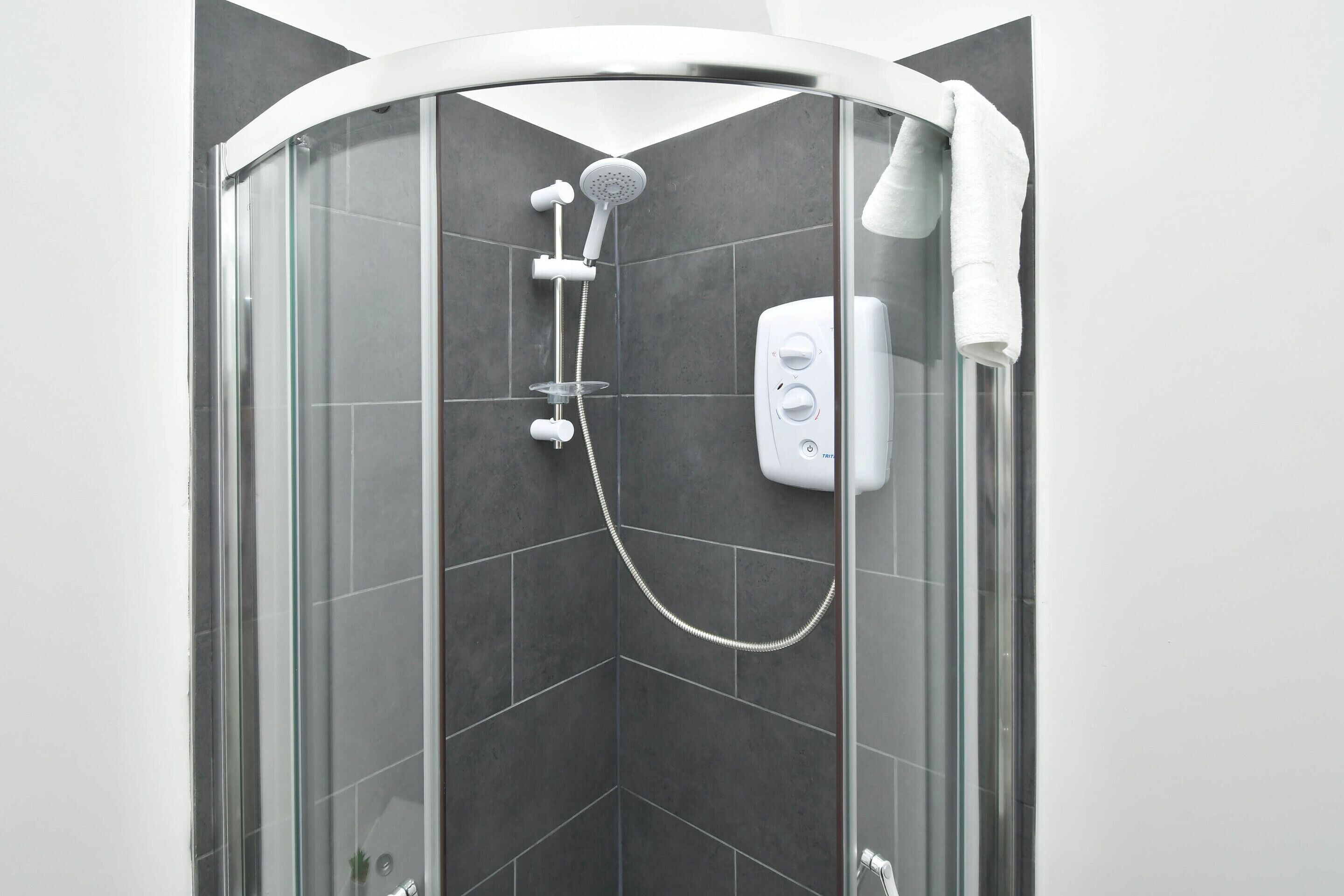 Une cabine de douche moderne dotée d’une porte en verre, d’un pommeau de douche à main, d’un panneau de commande fixé au mur et d’une serviette suspendue sur le côté droit.
