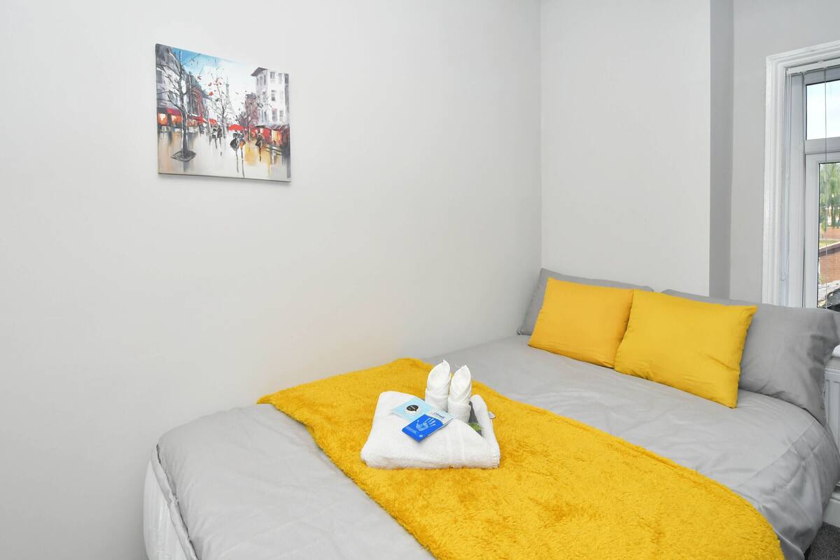 Ein Hotelzimmer mit Bett, gelbgrüner Tagesdecke, weißem Handtuch und einem Bild an der Wand.