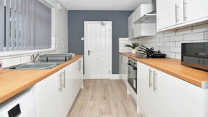 Une cuisine étroite avec des meubles blancs, des plans de travail en bois, un four encastré et une fenêtre équipée de stores.