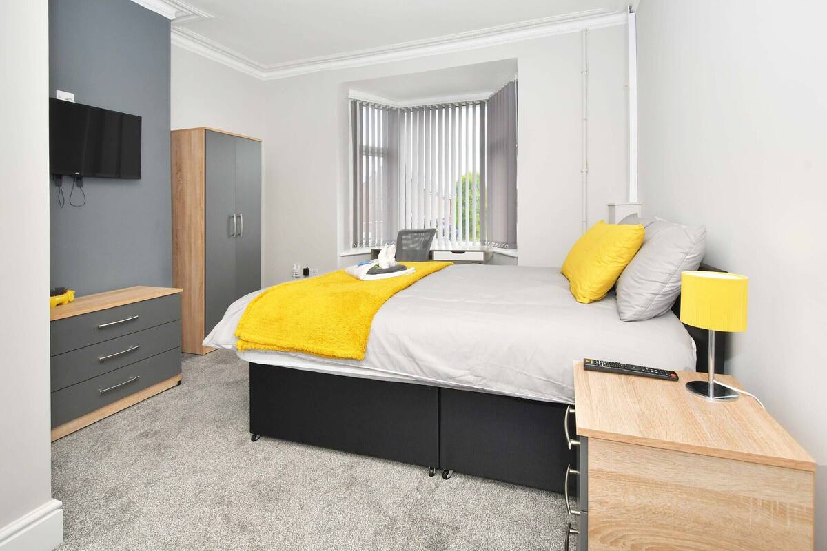 Ein modernes Schlafzimmer mit Bett, Nachttisch, Lampe und einem an der Wand befestigten Fernseher.