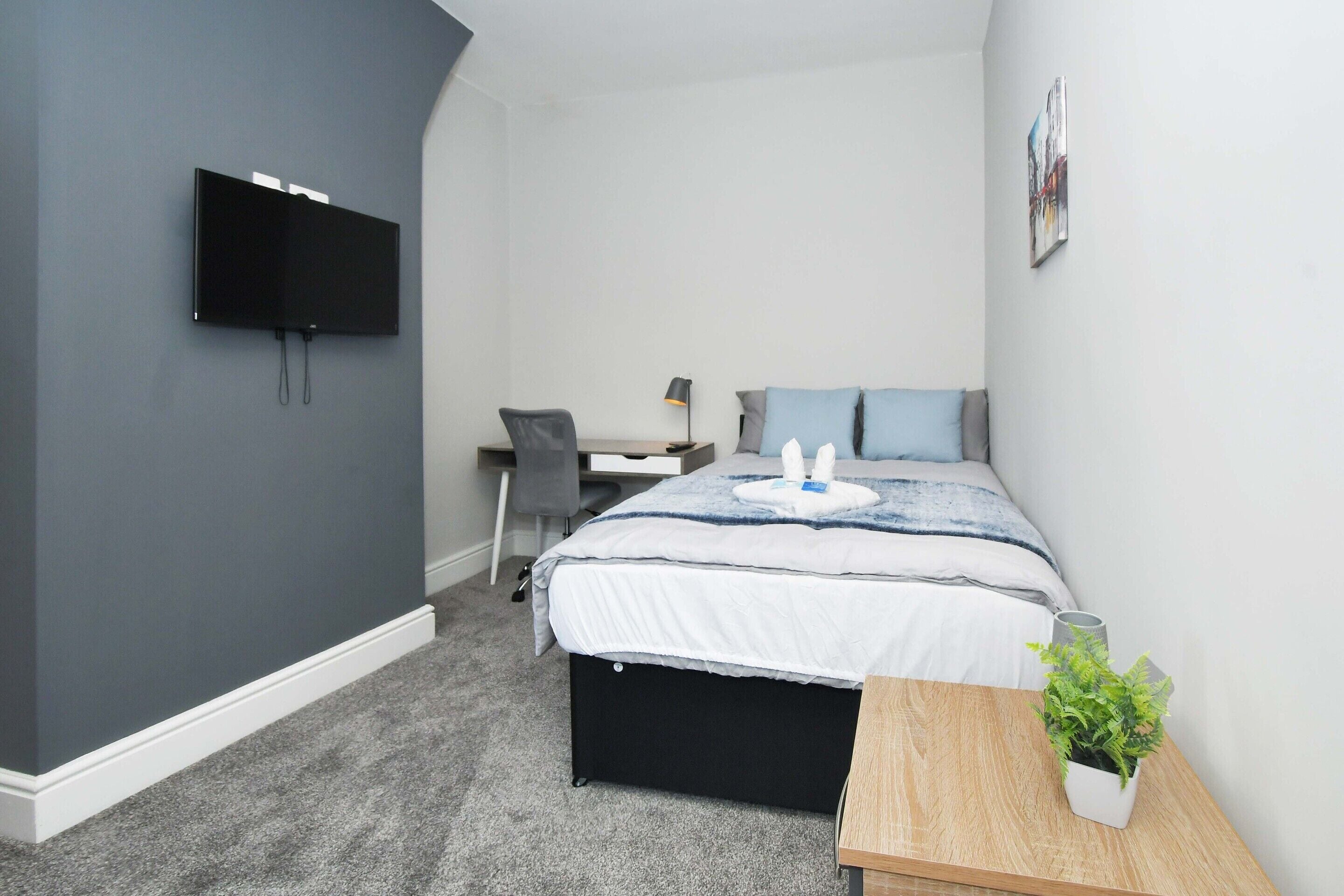 A bedroom with a bed, desk, chair, and a TV mounted on the wall.