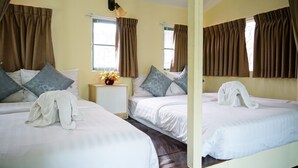 Ein Hotelzimmer mit zwei Betten, braunen Vorhängen, einem kleinen Tisch mit Blumenvase und einem Fenster.