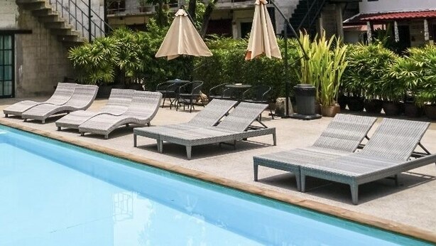 Ein Schwimmbecken mit Liegestühlen, Topfpflanzen und einem Gebäude mit nummerierten Türen.