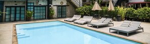 A swimming pool with lounge chairs, potted plants, and a building with numbered doors. - Town Home by The Warehouse Chiang Mai (Chiang Mai)