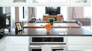 A modern kitchen with white cabinetry, a central island with a vase of flowers, and a built-in oven. - “El Castellito” on the Llano River [4 Bed House] (Llano)