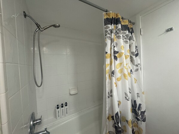 Une salle de bain avec une douche, une baignoire et des toilettes. Trois produits de toilette sont accrochés au mur : un gel douche, un après-shampoing et un shampoing.