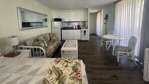 A compact living space with a kitchenette, a sofa, a dining table with chairs, and a large window with curtains.