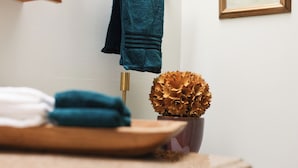Un baño con lavamanos de madera, un perchero con una toalla azul y un jarrón decorativo con flores doradas.