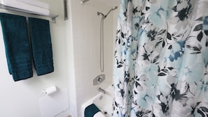 Un baño con ducha, bañera y retrete. Hay toallas colgadas en un perchero y una cortina de baño con estampado floral.