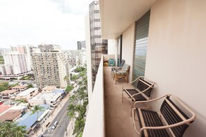 A balcony with two wicker chairs and a small table, overlooking a cityscape with tall buildings and palm trees. - 💎LOCATION💎 5min to 🏄‍♀️🏊‍♀️🐠🦈🌸 free parking 🚙🅿️, fast WIFI💻 🌺F18A01🌺 (Honolulu)