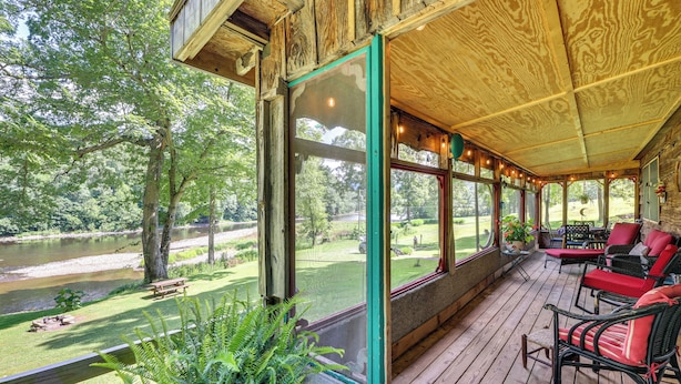 Une terrasse en bois avec des sièges extérieurs, offrant une vue sur une rivière et une zone verdoyante avec des arbres.
