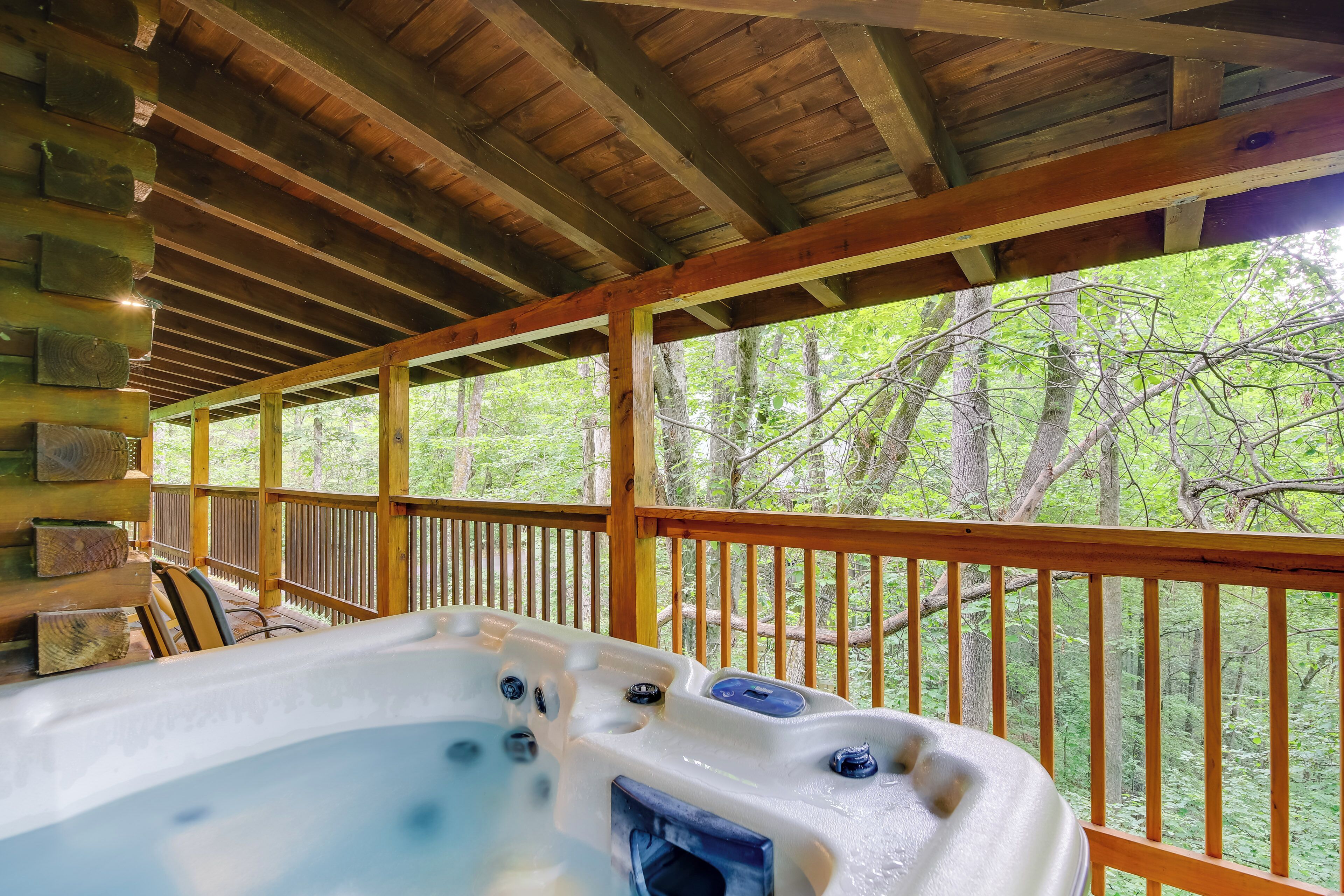 A wooden deck with a hot tub, stone walls, and a view of trees.