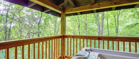 A wooden deck with a hot tub, surrounded by a forested area.