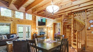 A wooden cabin interior with a dining area, a fireplace, a TV, and a spiral staircase. - Hot Tub + Pool Table: Secluded Seiverville Cabin (Sevierville)