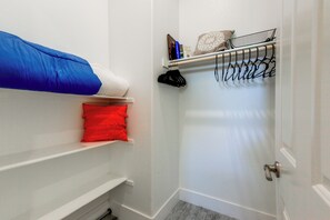 A small, narrow hallway with a white door, a shelf with a blue pillow, a red pillow, and a black hanger rack with clothes.