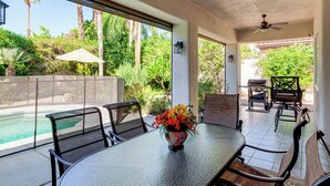 Un patio exterior con piscina, sillas de comedor, una mesa con un jarrón de flores y una parrilla.