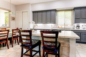 A kitchen with dark cabinets, a white countertop, and a central island with chairs.