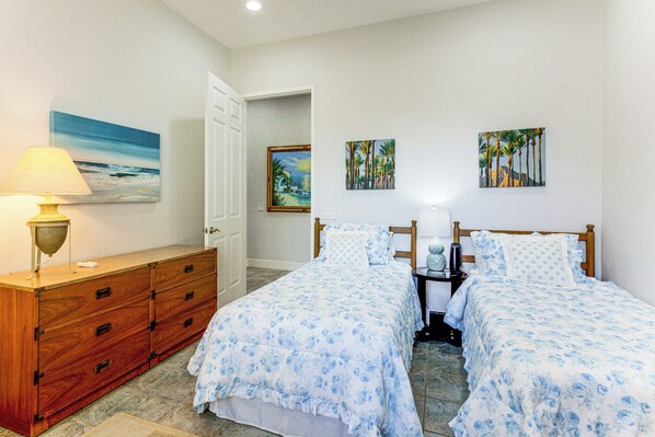 A bedroom with two beds, a dresser, a lamp, and three paintings on the wall.