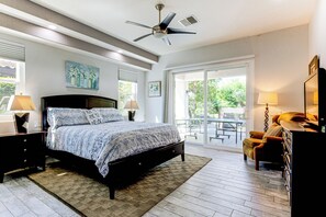 Un dormitorio con cama, lámparas de noche, ventilador de techo y vistas al exterior a través de un ventanal corredero.