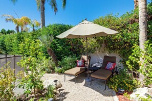 A patio with two lounge chairs, a table, and an umbrella.