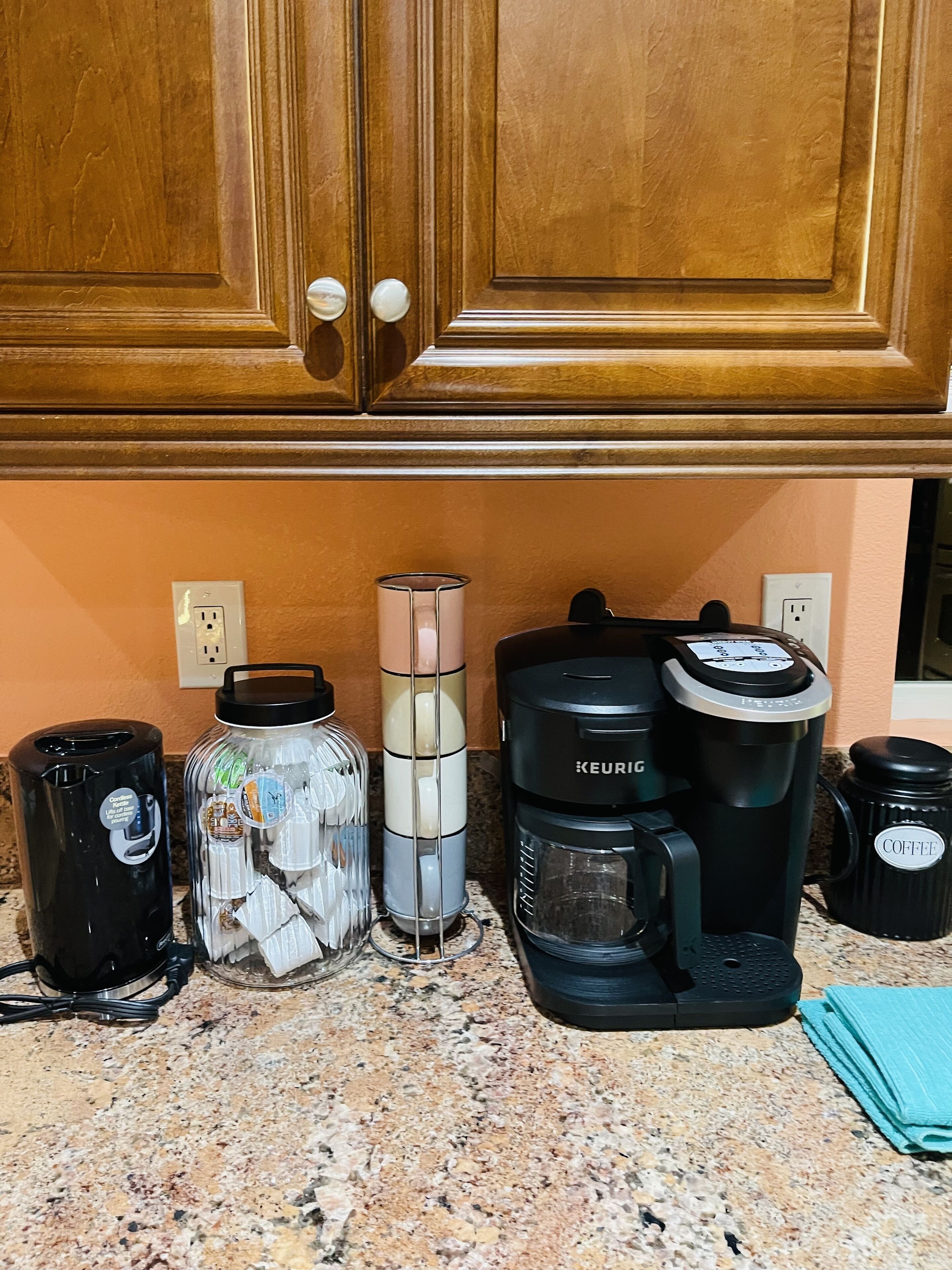 A kitchen counter with a coffee maker, a jar of coffee pods, a water dispenser, and a coffee mug.
