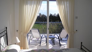 A bedroom with a bed, a balcony with chairs, and curtains.