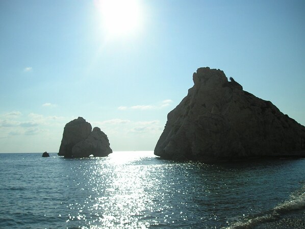A clear view of two large rock formations in the sea with a bright sun in the background.