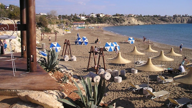 A beach with umbrellas, lounge chairs, and a wooden structure.