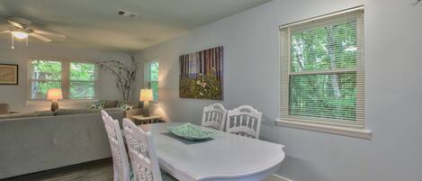 A dining area with a white table and chairs, a ceiling fan, and a window with blinds.