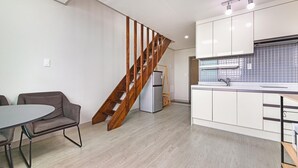 Une cuisine moderne avec des meubles blancs, un réfrigérateur gris et un escalier en bois.