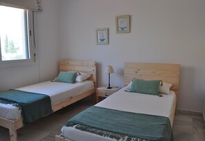 Two single beds with wooden headboards, a bedside table with a lamp, and two framed pictures on the wall.