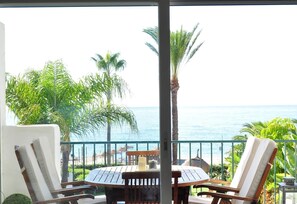 A balcony with a table and chairs, overlooking a beach and palm trees.
