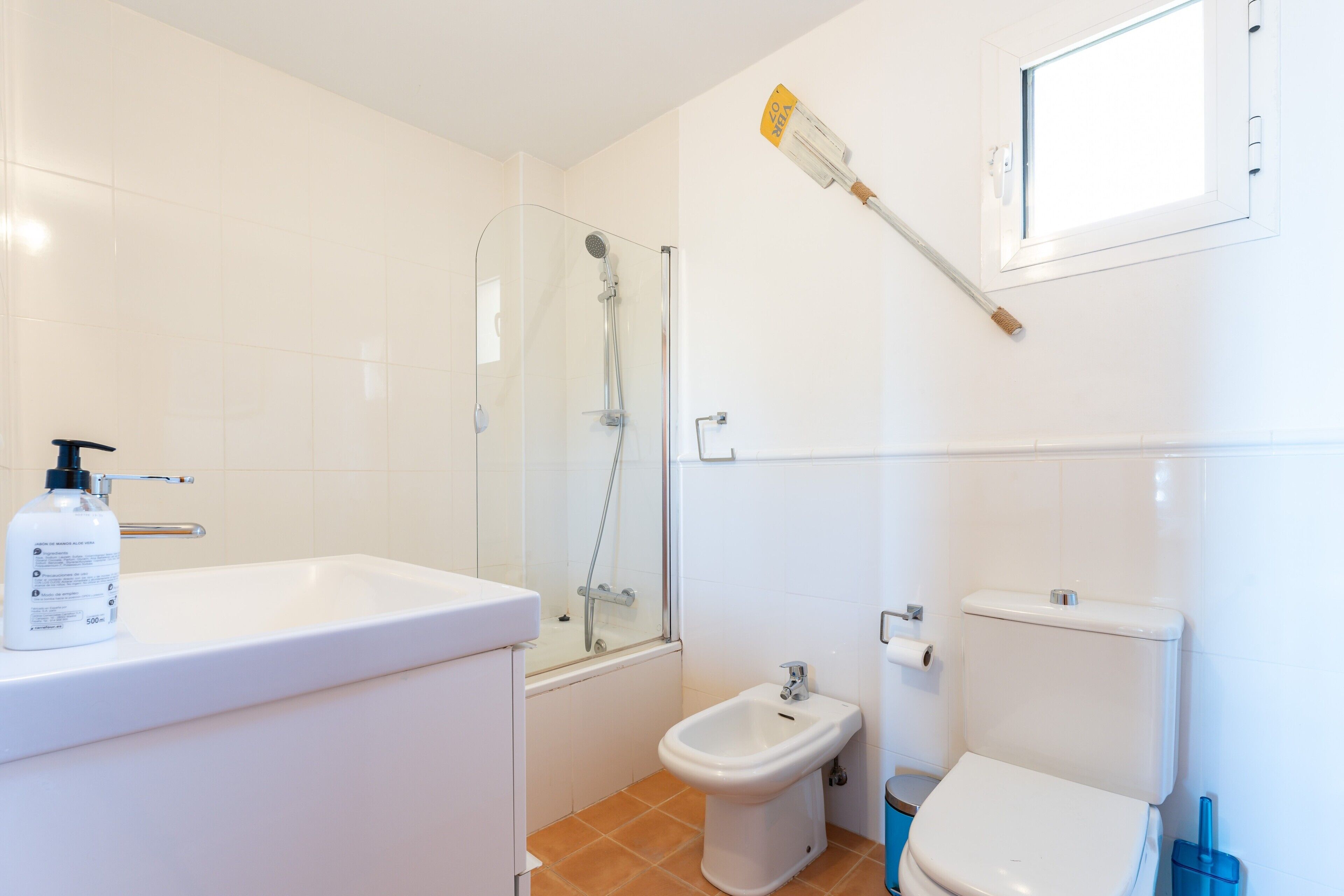 Et badeværelse med bruser, bidet, toilet og en håndspritflaske på vasken.