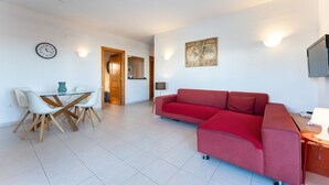 Un salon moderne avec un canapé rouge, des fauteuils blancs, une table en verre, une horloge murale, une carte et un téléviseur.