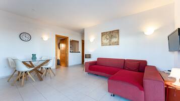 A modern living room with a red sofa, white chairs, a glass table, a wall clock, a map, and a TV.