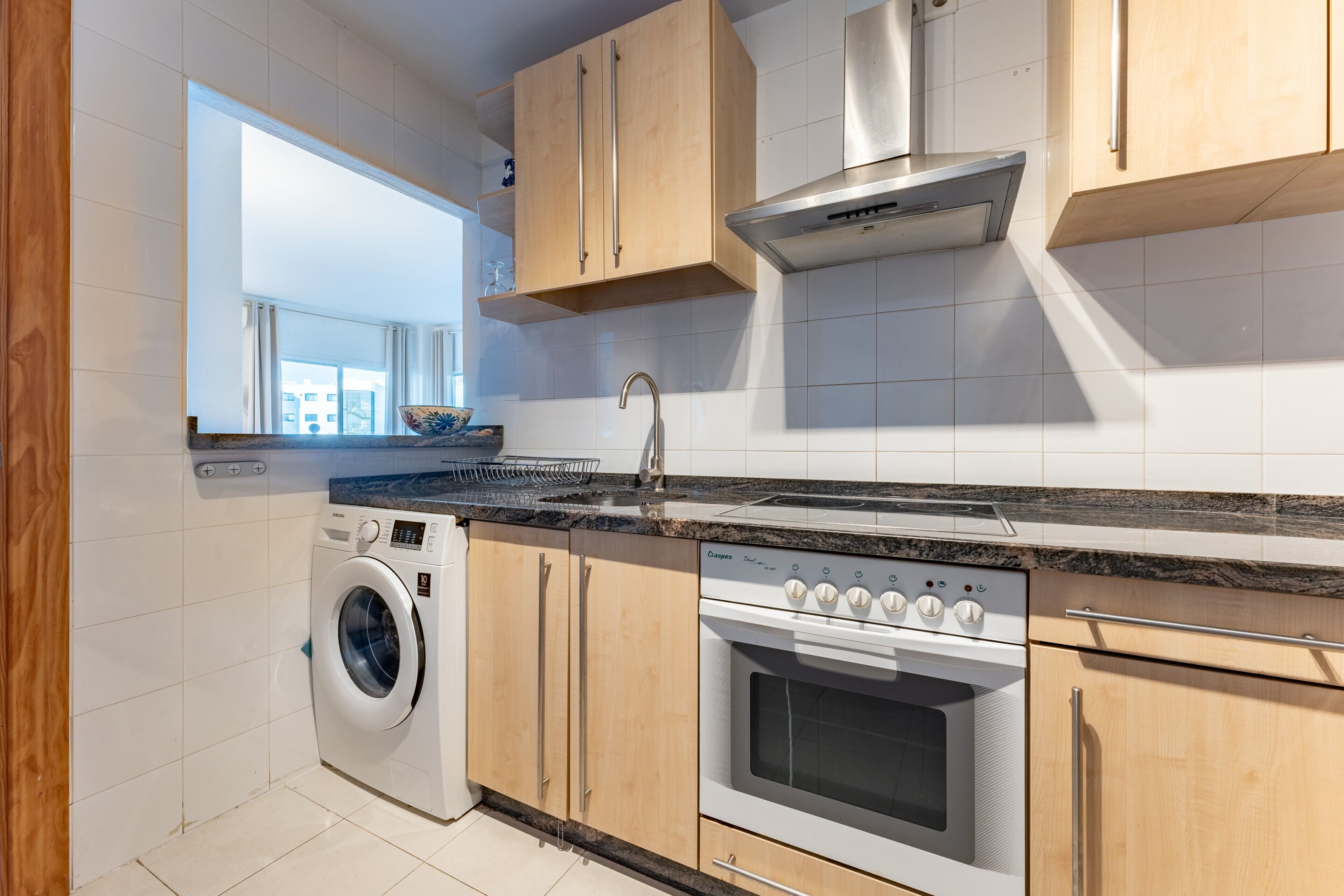 A modern kitchen with a washing machine, oven, and stainless steel range hood.