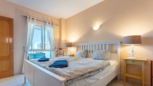 Une chambre à coucher avec un lit, des tables de chevet, une fenêtre avec des rideaux et une vue sur les bâtiments à l’extérieur.