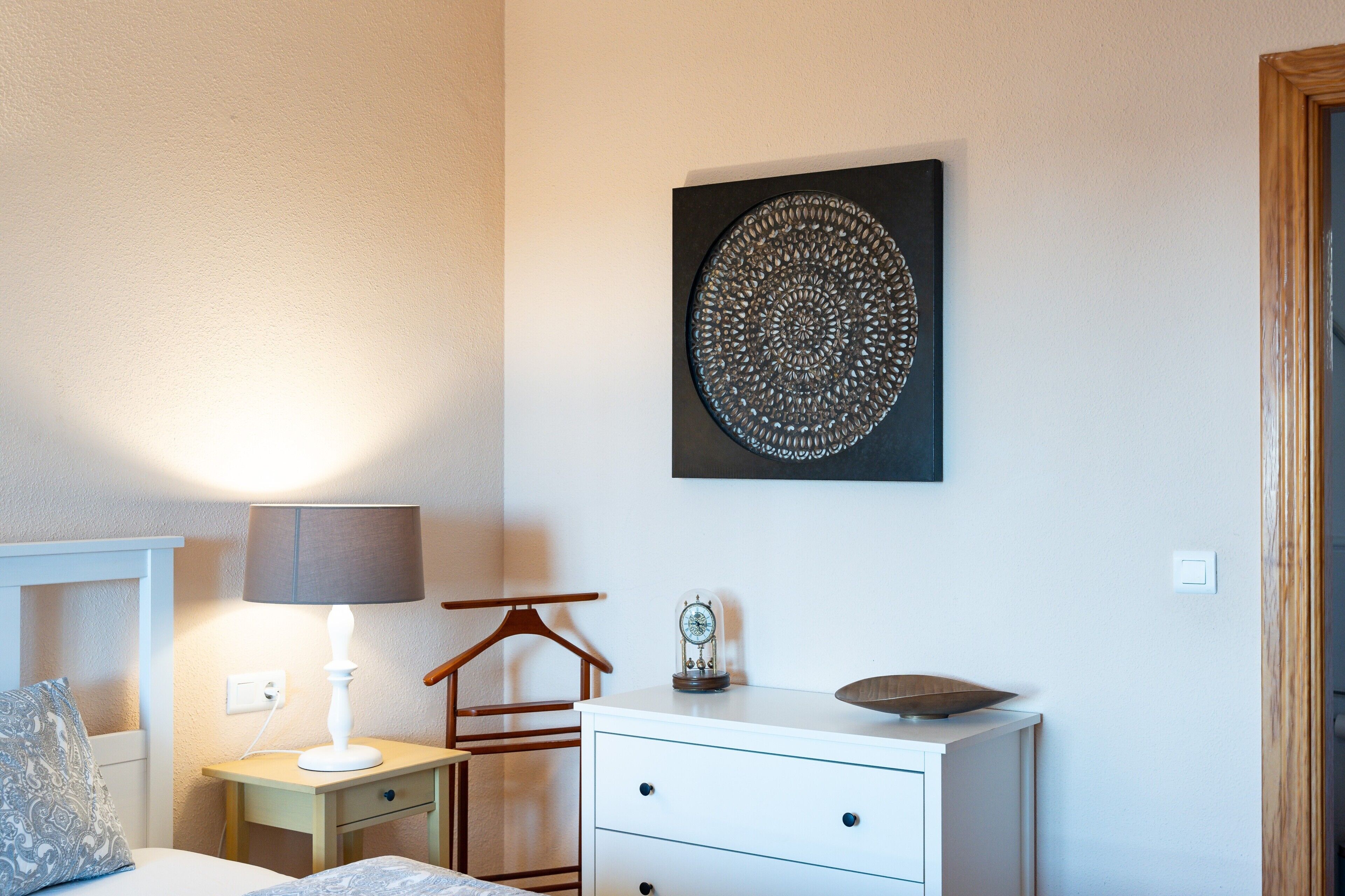 Une chambre à coucher comprenant un lit, une table de chevet, une lampe, une commode et une assiette décorative fixée au mur.