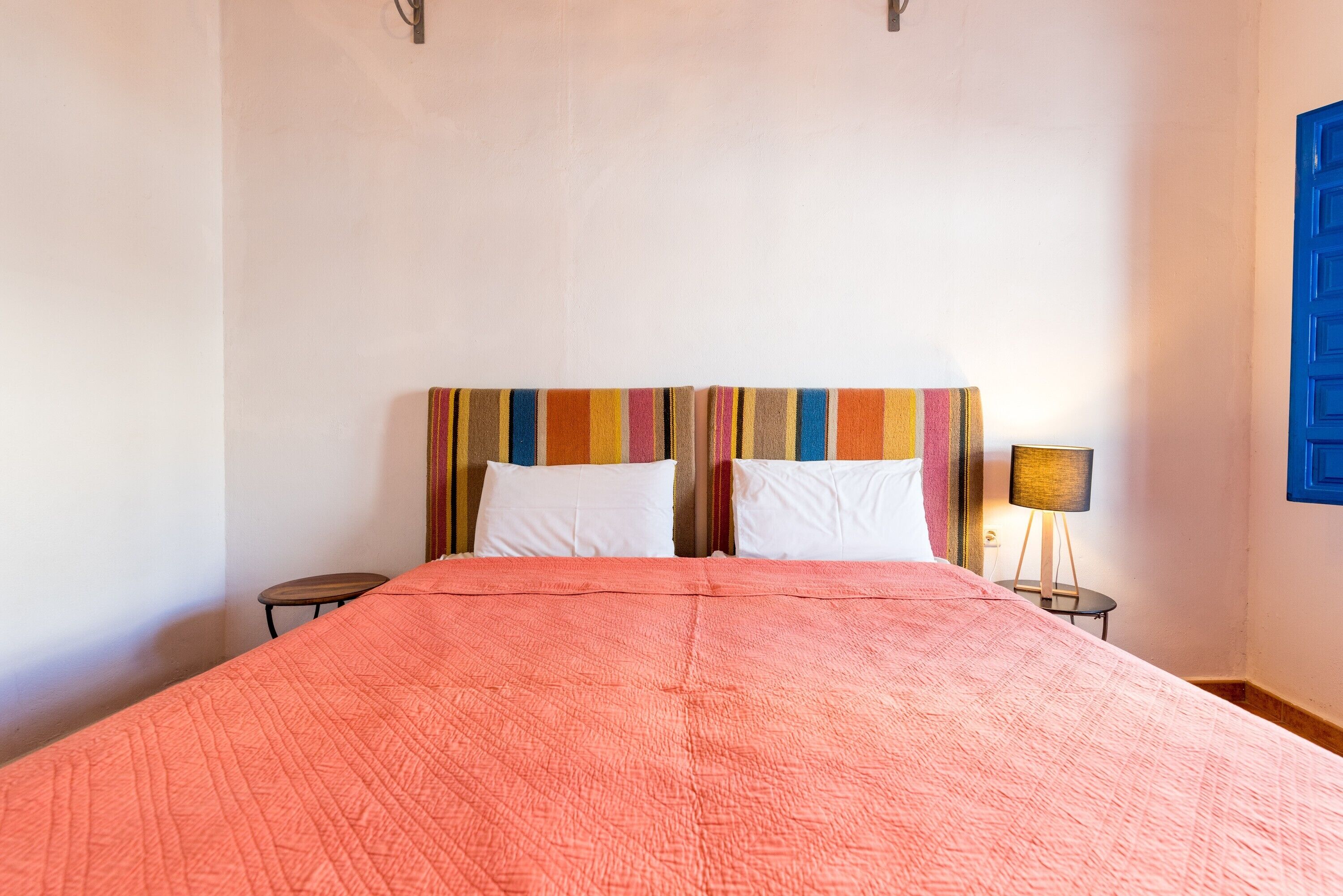Un lit double avec une couette rose, deux oreillers blancs et une tête de lit rayée aux couleurs vives.