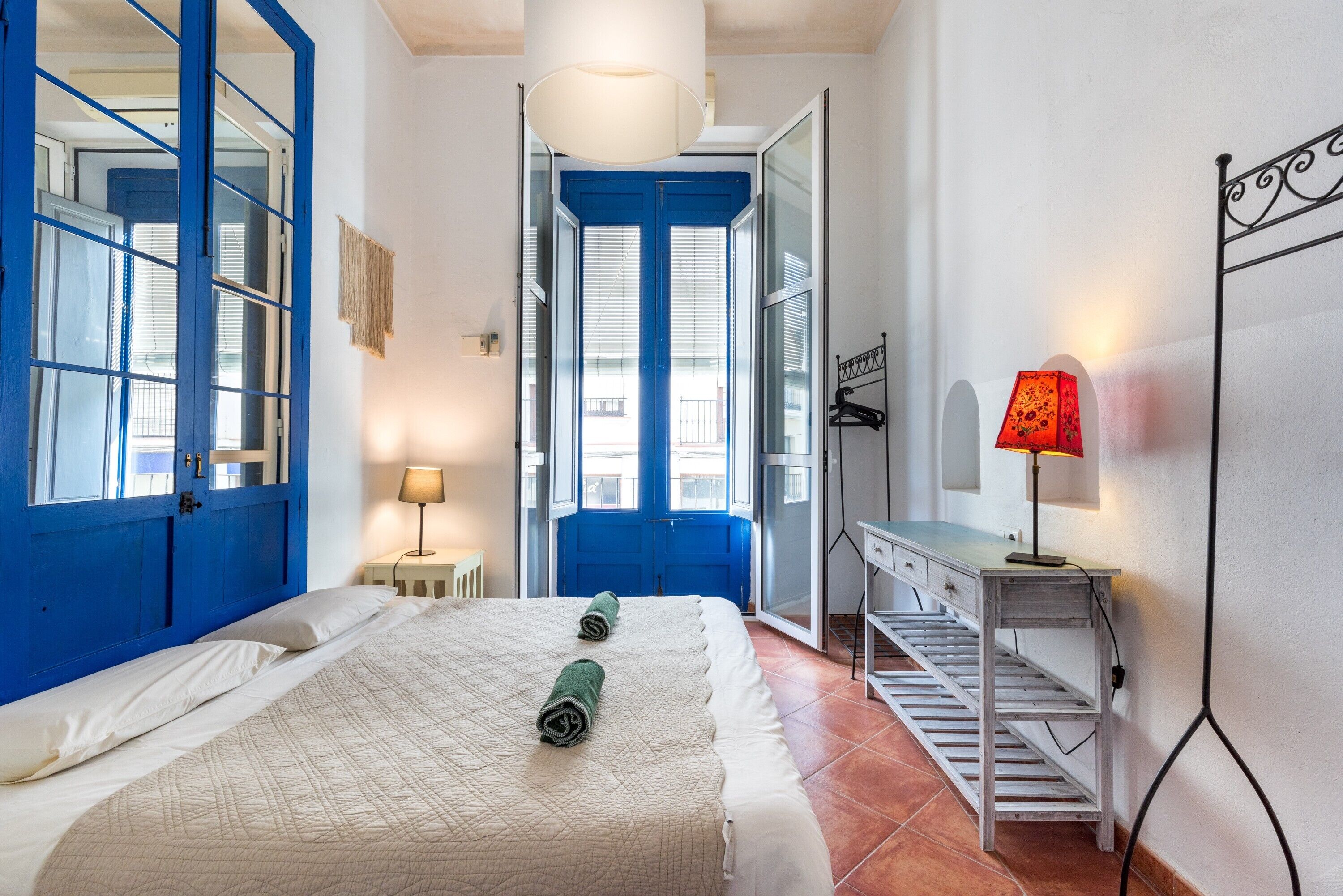 A bedroom with a bed, a desk, a lamp, and a view through a blue door.